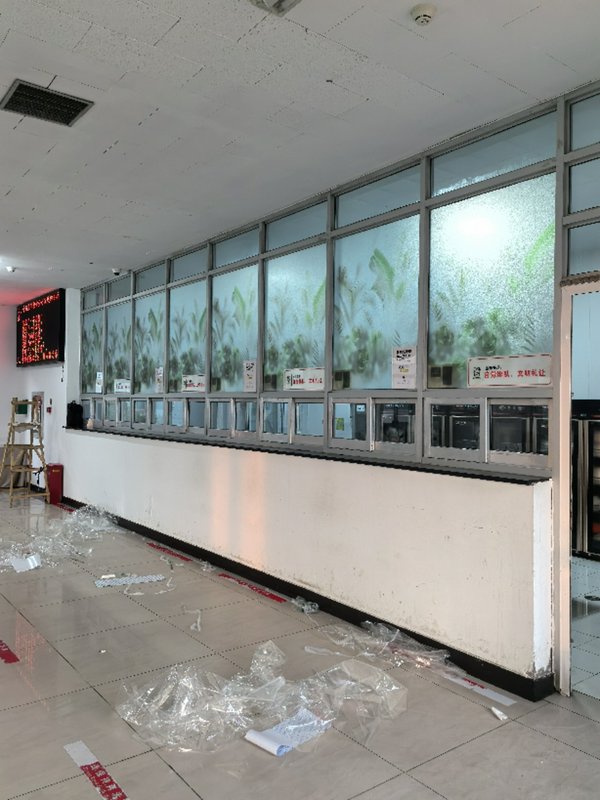 Long row of teller windows in an empty, vandalized lobby with scattered debris on tiled floor