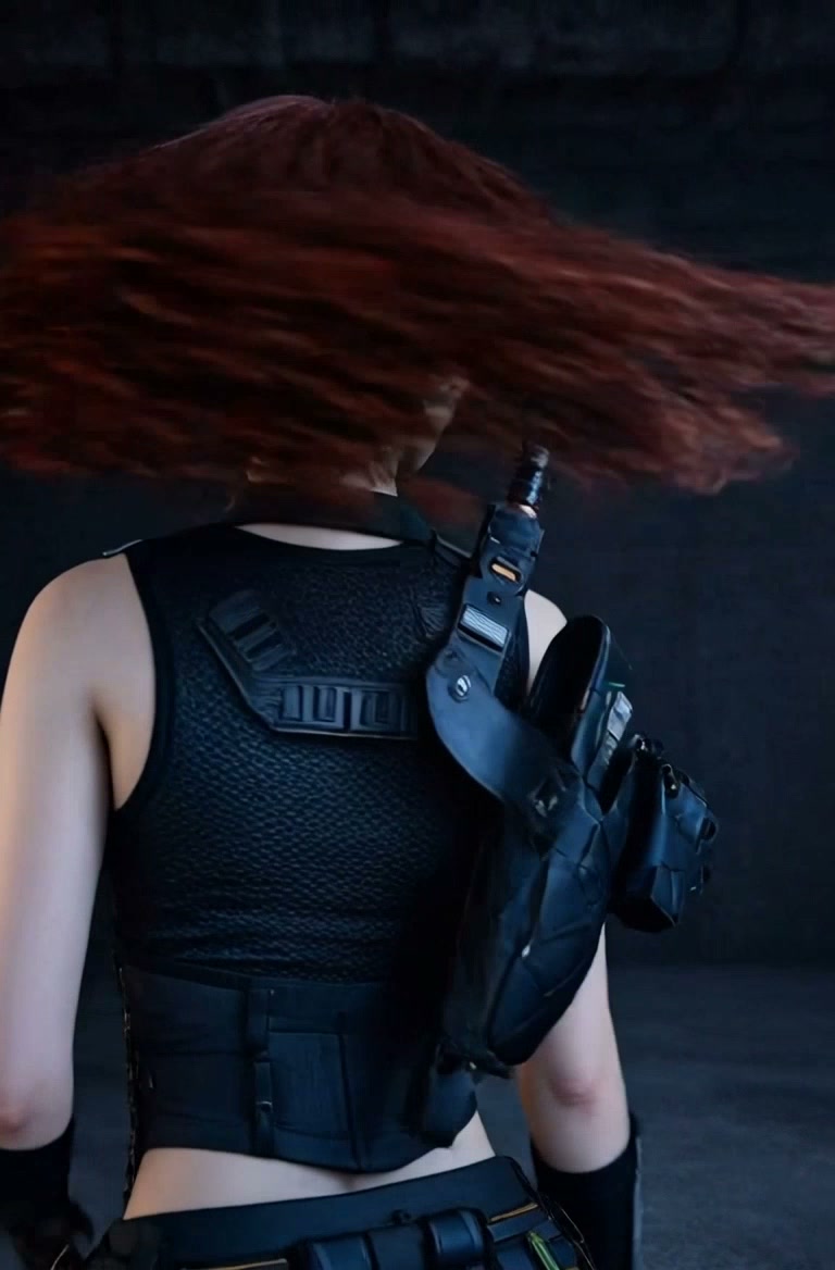 Back view of a person with wind-swept red hair, wearing a black tactical vest and gear.