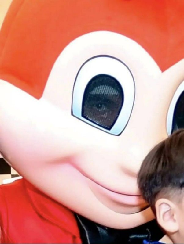 Close-up of a large cartoon mascot head with red hair beside a child's head.