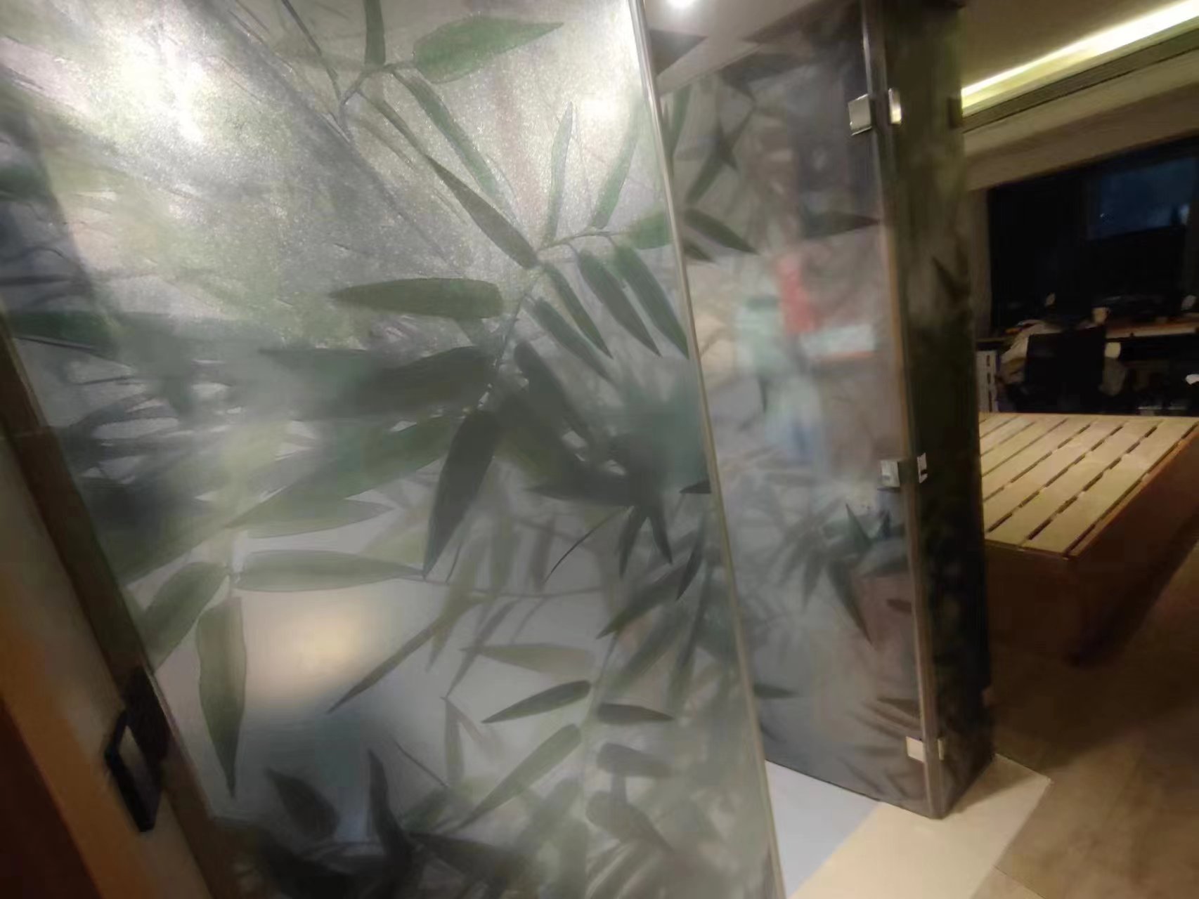 Frosted glass privacy divider with bamboo leaf pattern in a modern interior space.