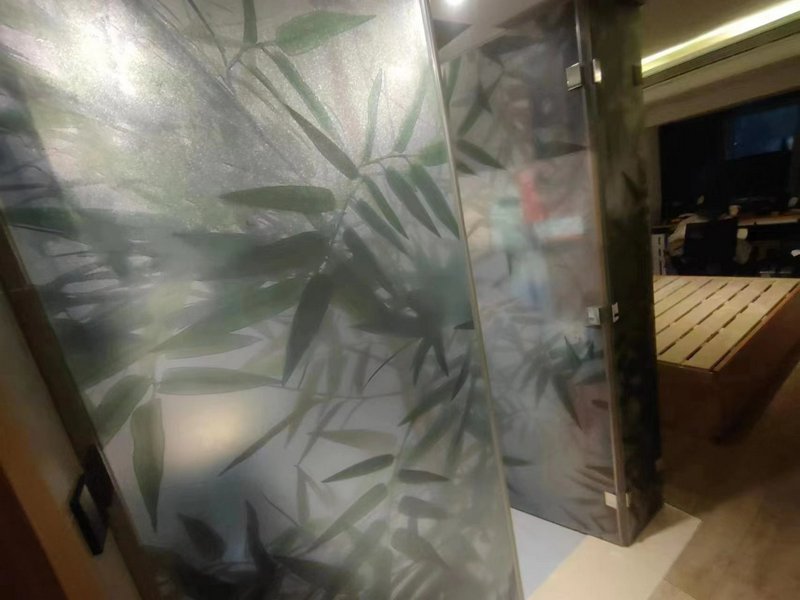 Frosted glass privacy divider with bamboo leaf pattern in a modern interior space.