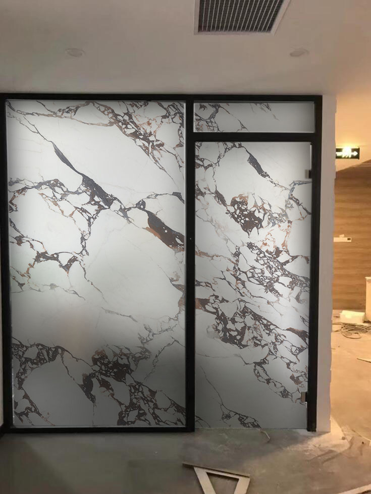 Interior partition with large marble-pattern frosted glass panels in black frames.