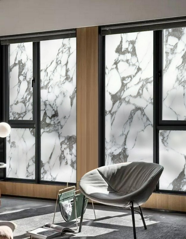 Modern interior with marble walls, black-framed windows, and a grey lounge chair.