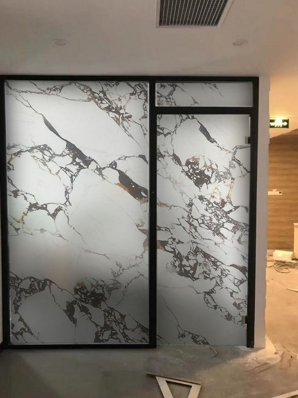 Interior partition with large marble-pattern frosted glass panels in black frames.
