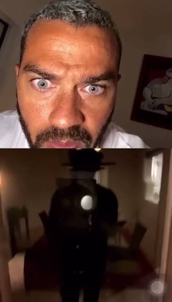 Close-up of a surprised man with a dark, shadowy figure in a dim room.