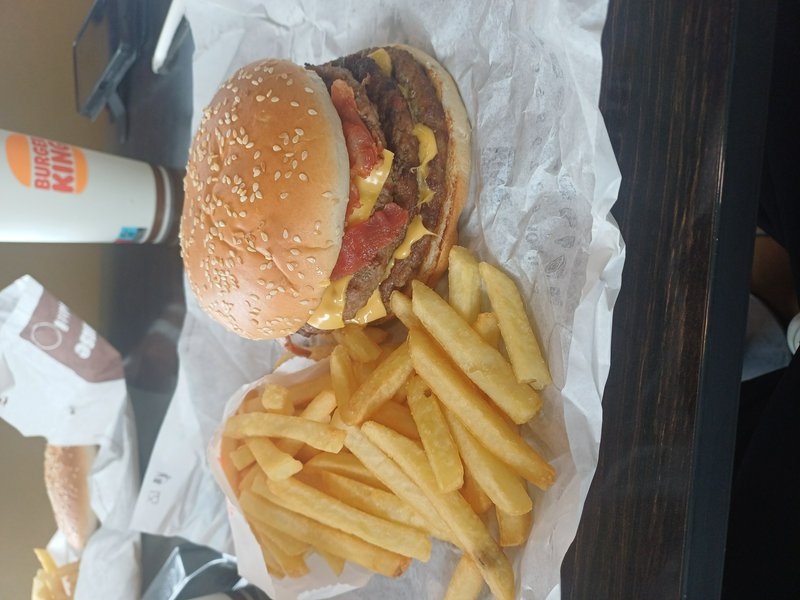 Close-up of stacked Burger King cheeseburger, golden french fries, and branded drink on a dark wo...