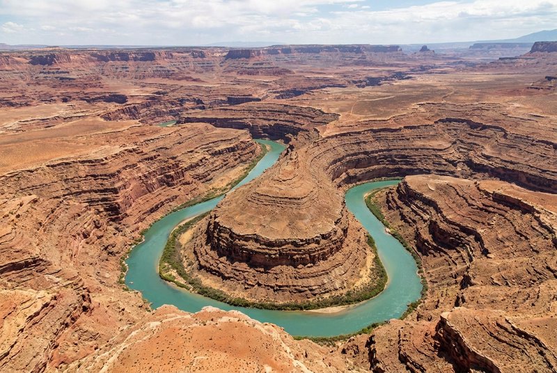[High-angle view of a meandering turquoise river carving through layered red rock desert canyons under a partly cloudy sou...