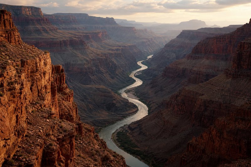 High angle view of Grand Canyon, winding Colorado River snaking through red rock cliffs at golden hour sunset.