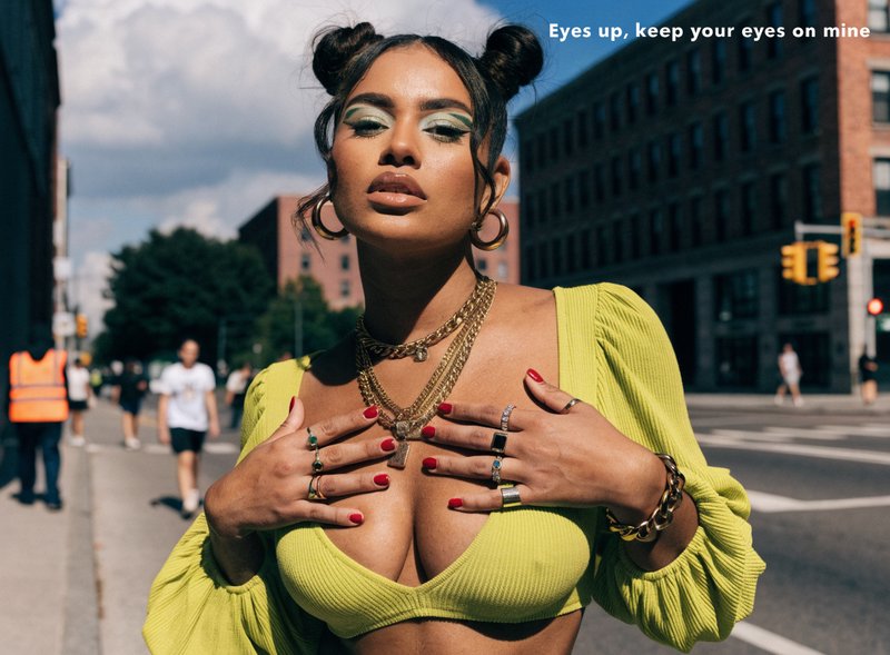 Fashionable woman with double space buns, lime green top, stacked gold jewelry poses on a sunny d...