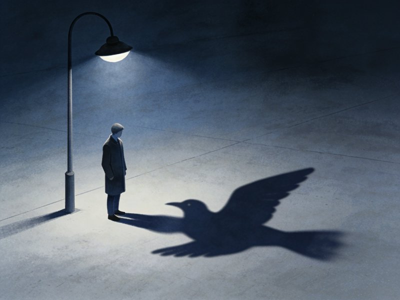 Man standing under a glowing streetlight stares at his large bird-shaped shadow on empty concrete...