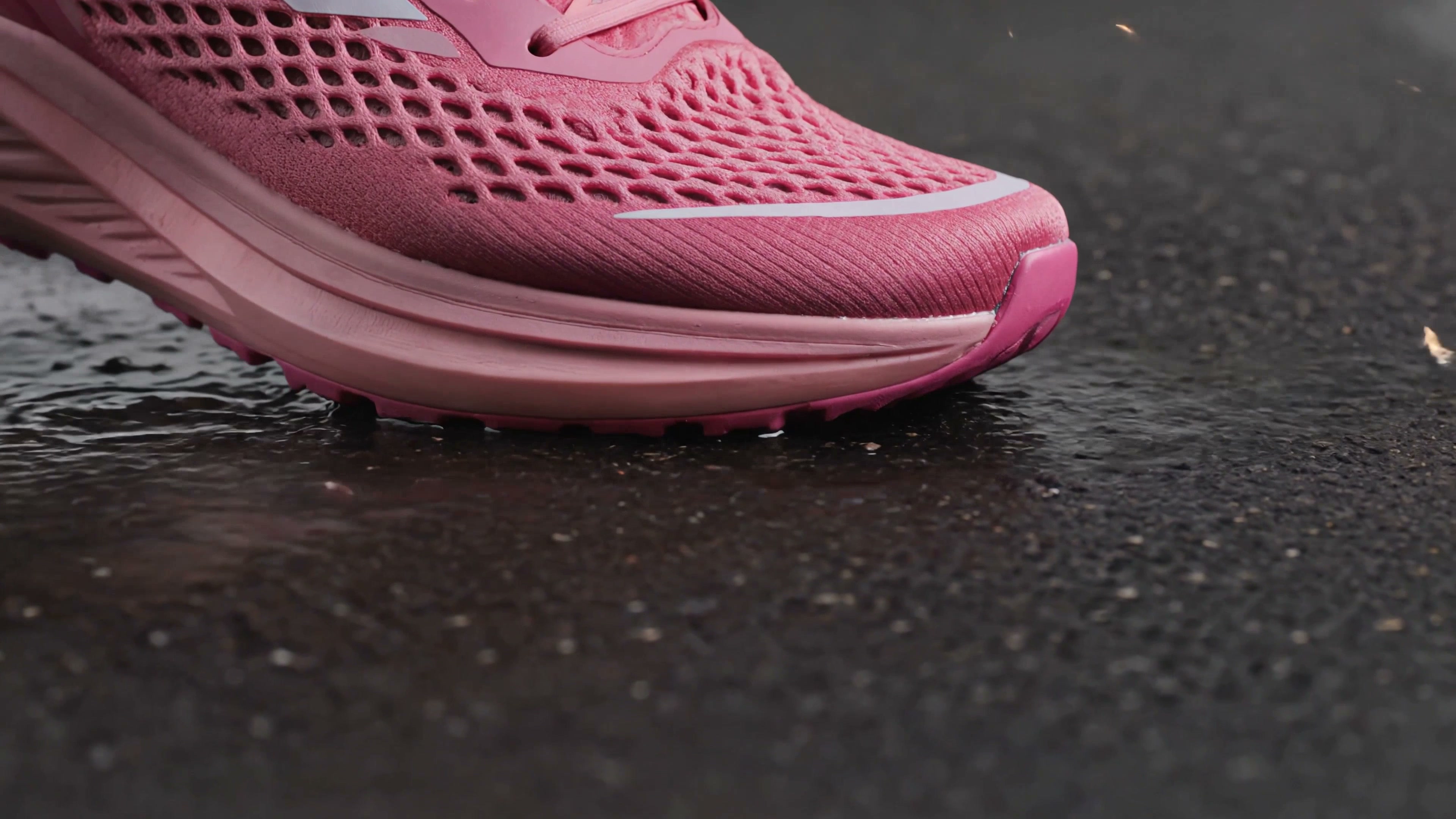 Pink running shoe close-up on wet pavement showing mesh upper and textured sole.