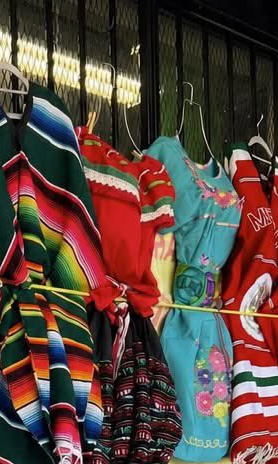 Colorful traditional garments on hangers in a store display featuring striped ponchos and floral dresses.
