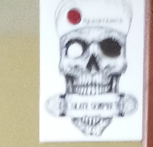 Blurry grayscale skull sticker with a red dot on the forehead mounted on a light wall.