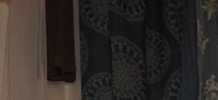 Dark patterned curtain with circular mandala motifs beside a beige wall and brown fabric.
