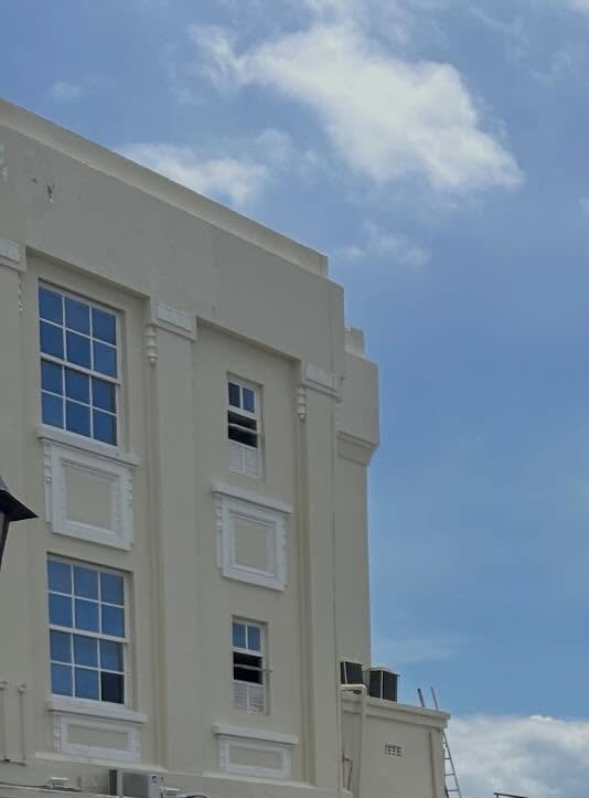 Close-up of a pale beige multi-story building facade with decorative pilasters and grid windows against a blue sky.
