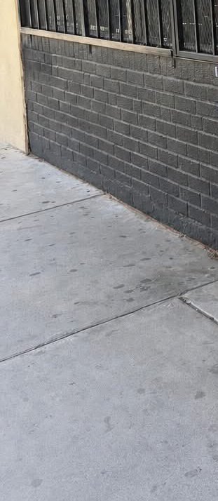 Concrete sidewalk beside a dark gray brick wall with barred windows.