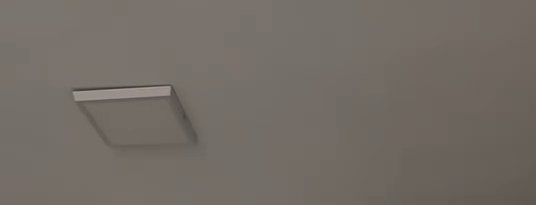 Low angle view of square flush mount ceiling fixture set into a plain warm taupe interior ceiling