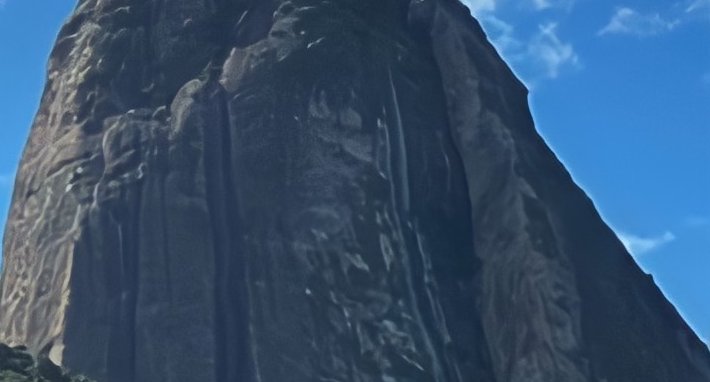 Low angle view of a towering sheer rocky cliff face against a bright clear blue sky with faint wi...