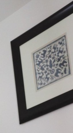 Framed folk art print with stylized blue animal motifs, matted and hung on a plain white interior...
