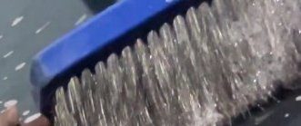 Close-up of a sudsy stiff bristle scrub brush with a bright blue plastic handle held above a work...