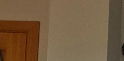 Close up of residential room corner showing light beige walls and partial edge of warm brown wood...