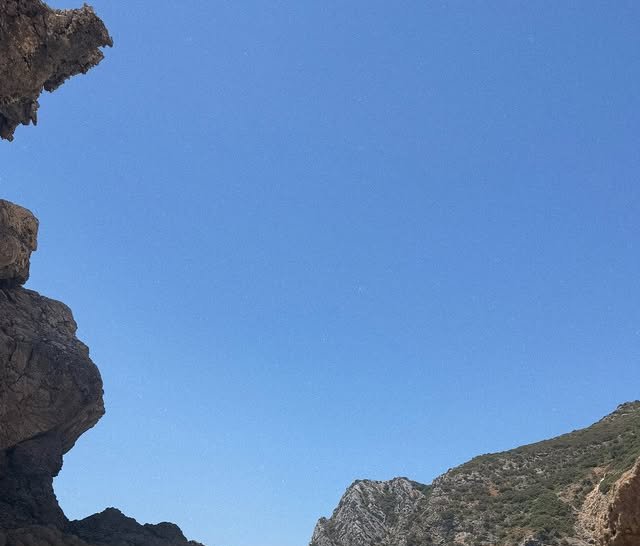Jagged eroded rock formations frame a wide, cloudless bright cerulean sky on a sunny arid day.