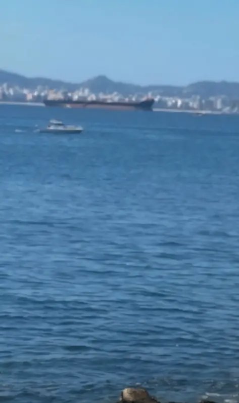 Rippled blue coastal ocean with a small motor yacht, distant cargo ship, and hazy shoreline city ...