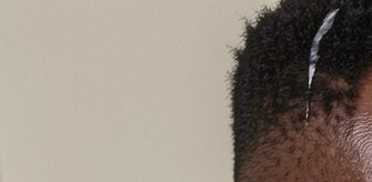 Close-up partial view of a person's short curly afro with a silver hair pick, against a plain lig...