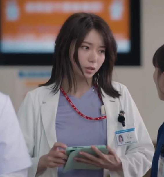 Young female doctor in white coat with ID badge holding a tablet in a hospital setting