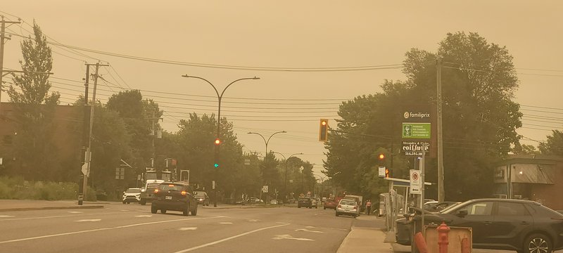 Orange hazy suburban intersection shrouded in thick wildfire smoke, with cars waiting at traffic ...