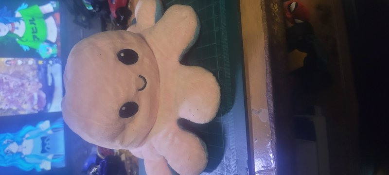 Light peach smiling octopus plush resting on a cluttered hobby work desk
