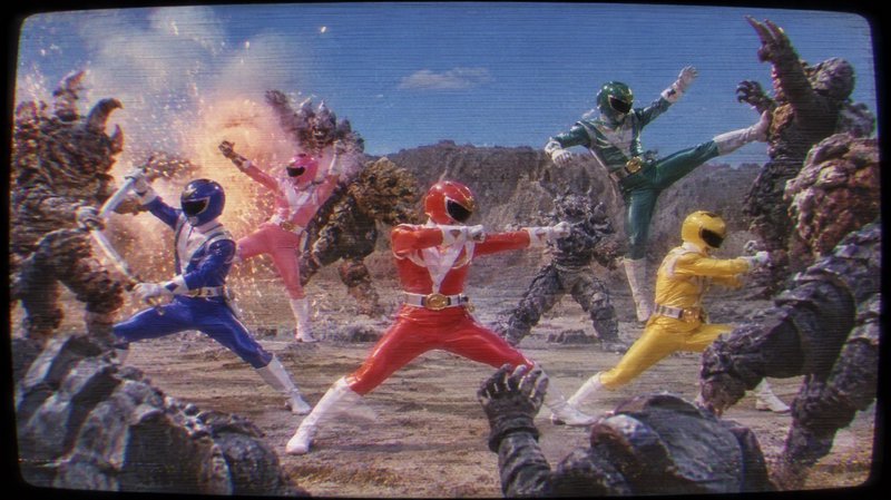 Costumed ranger team in bright colored suits battling rock monsters on a barren desert battlefield