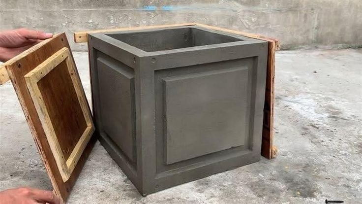A gray square concrete planter mold with a wooden lid being removed.
