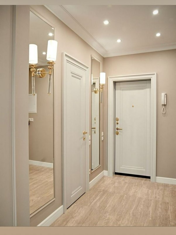 Bright modern hallway with beige walls, white doors, and mirrored panels.