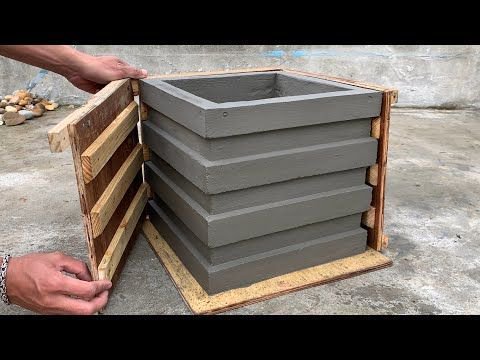 Hands open a wooden crate revealing stacked gray concrete planter molds inside.