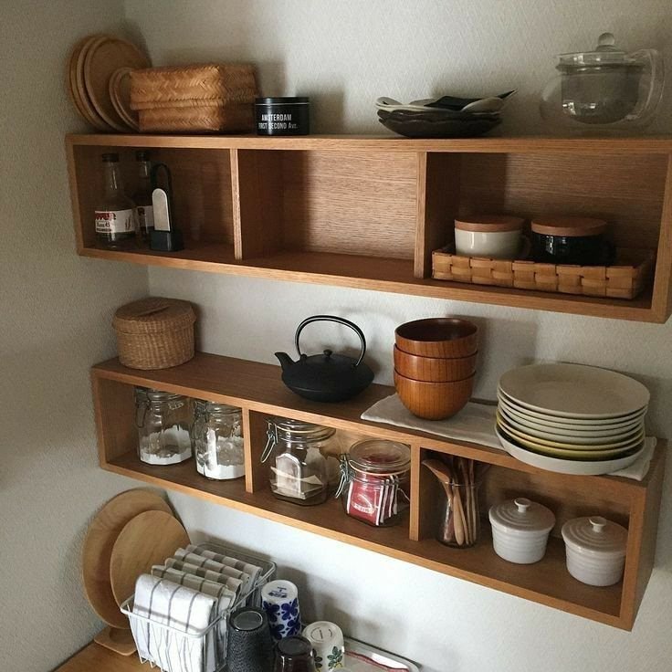 Open wooden wall shelves displaying teapot, jars, bowls, and plates in a cozy kitchen.
