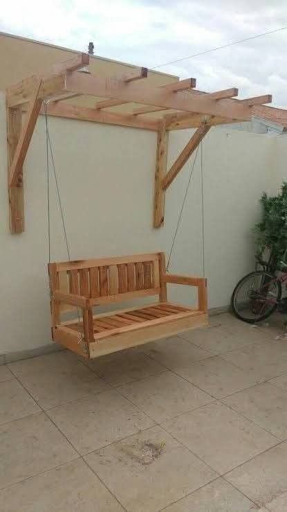Unfinished wooden wall-mounted pergola with a slatted hanging porch swing installed on a tiled re...