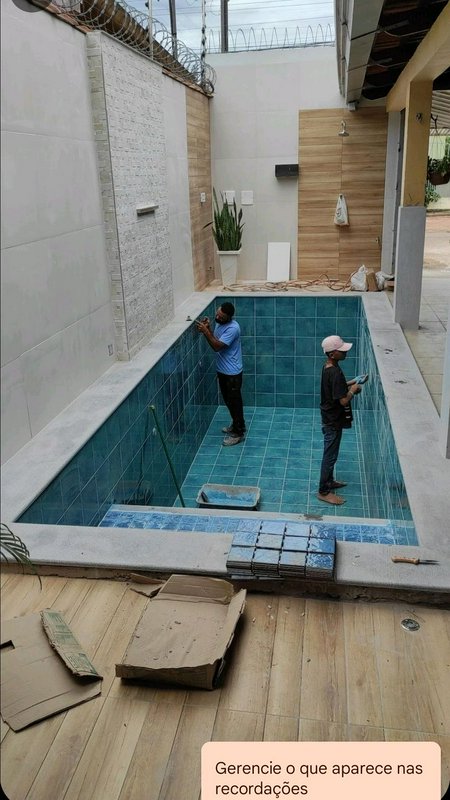 Two construction workers install teal ceramic tile inside a new enclosed residential swimming poo...