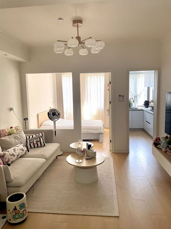 Sunlit cozy small apartment living room with cream furniture, open view to adjacent bedroom and c...