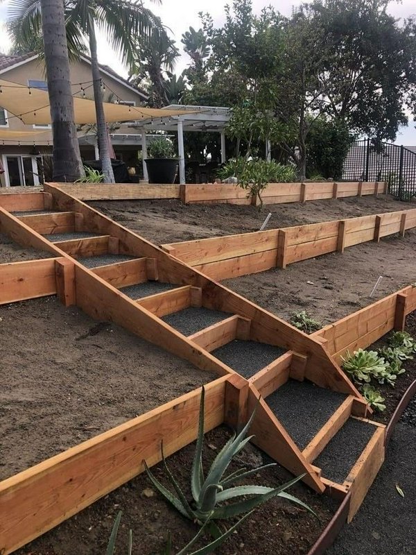 Newly built cedar terraced retaining wall with integrated gravel steps on a sloped residential ba...