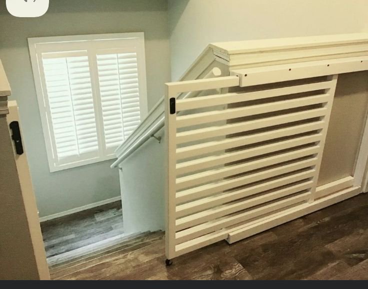 Poorly built DIY rolling white stair safety gate, incorrectly slanted to match the stair slope in...