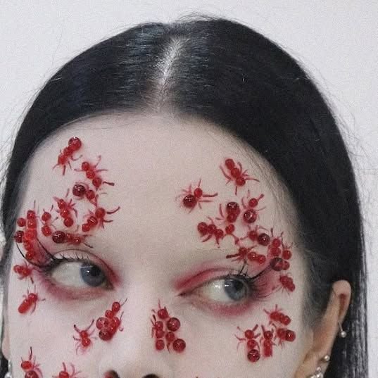 Close-up of surreal special effects makeup with 3D red ant decals clustered around the eyes on a ...