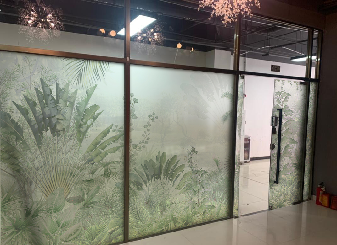 Frosted glass wall with tropical plant pattern and a glass door in an office hallway.