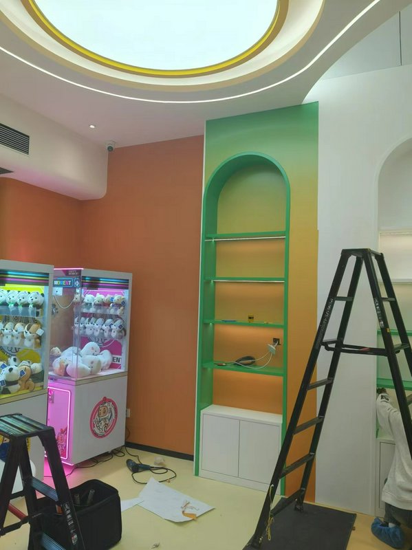 Colorful arcade room with claw machines, a green arched shelf, orange wall, and a black ladder.