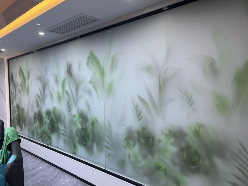 Frosted glass wall with green leafy plant silhouettes in an office hallway.