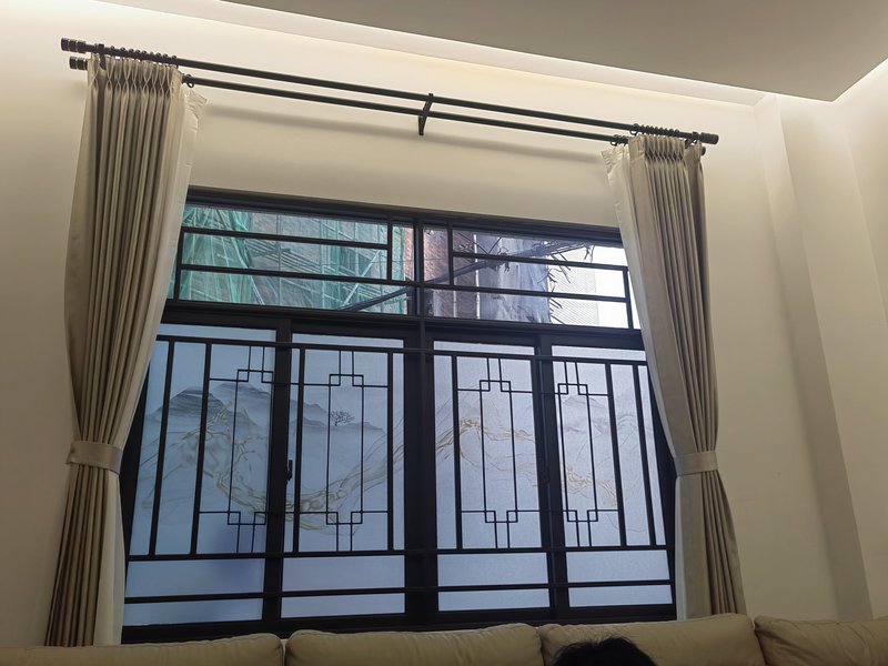 Beige curtains framing a decorative metal-framed window with frosted glass and mountain art.