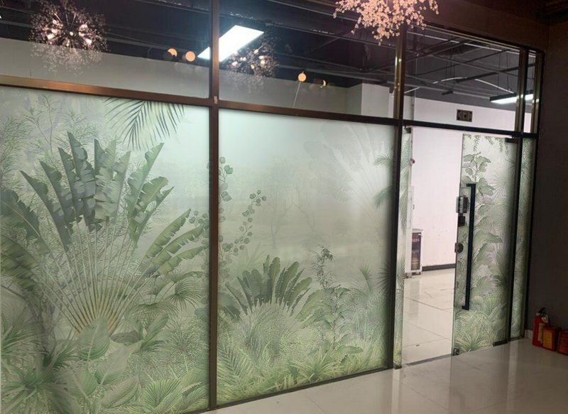 Frosted glass wall with tropical plant pattern and a glass door in an office hallway.