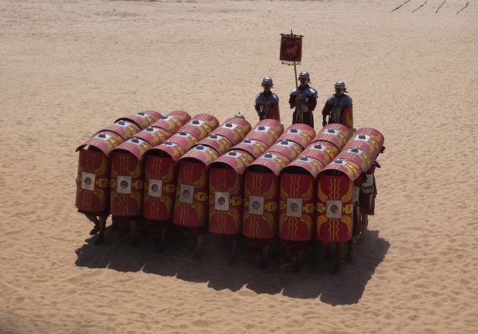 Group of armored soldiers forming a shield wall on a sandy desert.