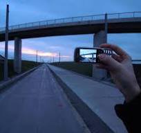 Hand holding an old mobile phone taking a photo of an empty paved road under a concrete overpass ...