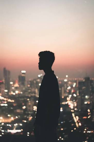 [Silhouette of a man in profile overlooking a blurred glowing city skyline at soft pink dusk sunset]